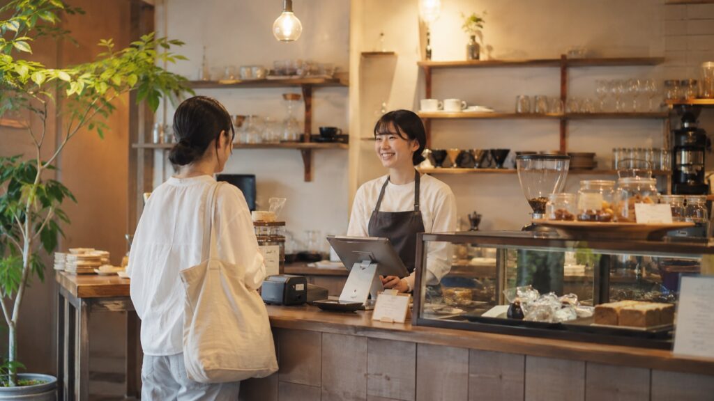 カフェのカウンターで会計をしながら談笑するスタッフとお客様(イメージ)